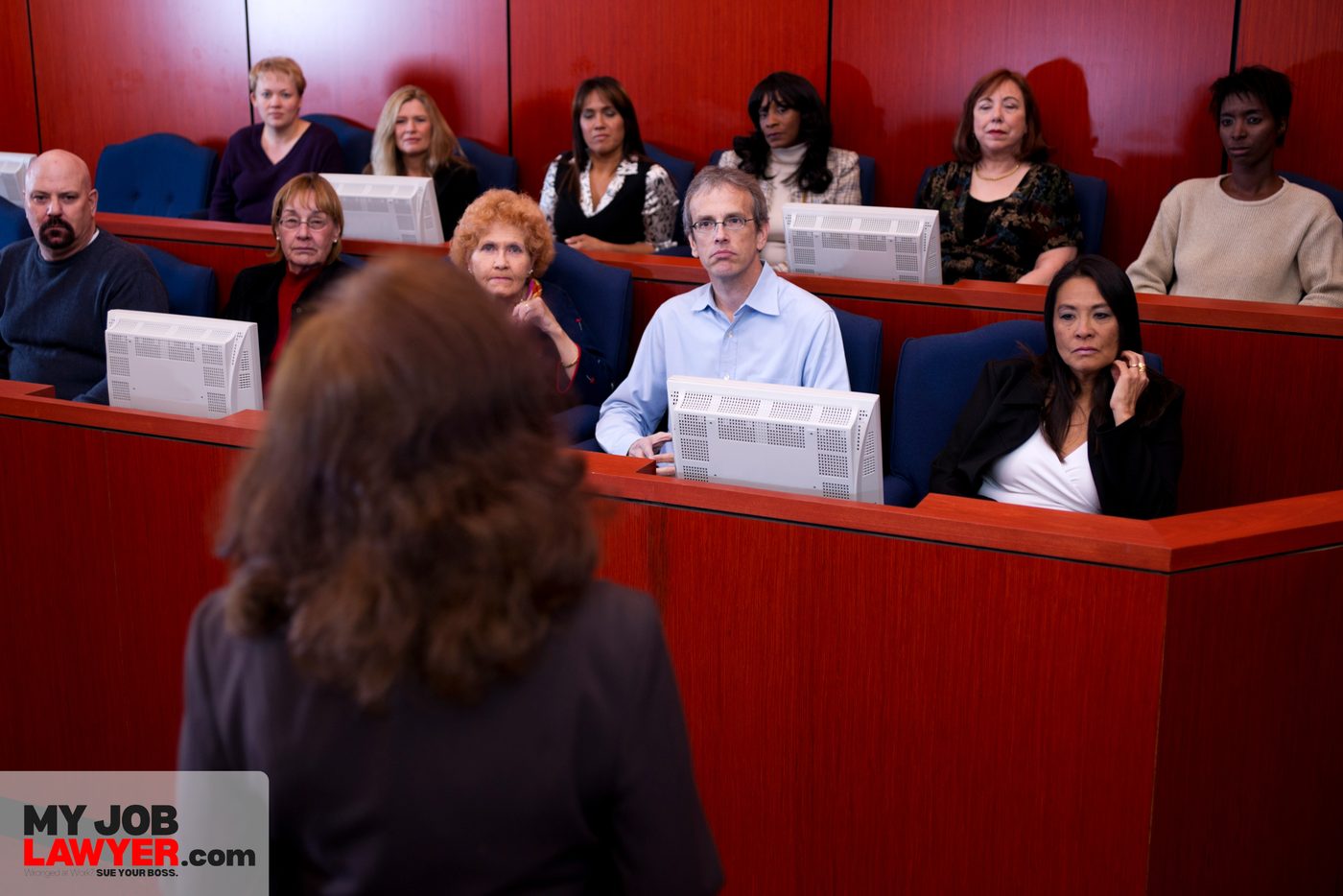 An attorney stands in a courtroom facing jurors seated in the jury box.